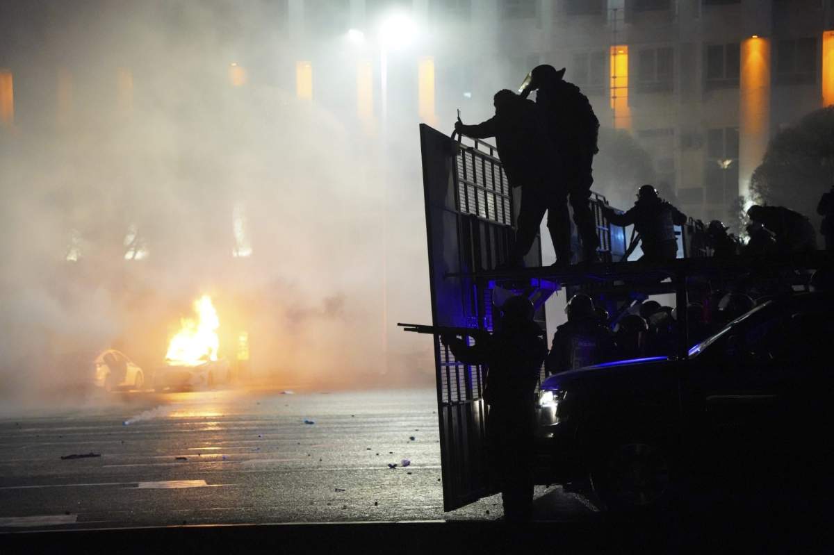 A police car on fire as riot police prepare to stop protesters in the center of Almaty, Kazakhstan, Wednesday, Jan. 5, 2022. (AP Photo/Vladimir Tretyakov)