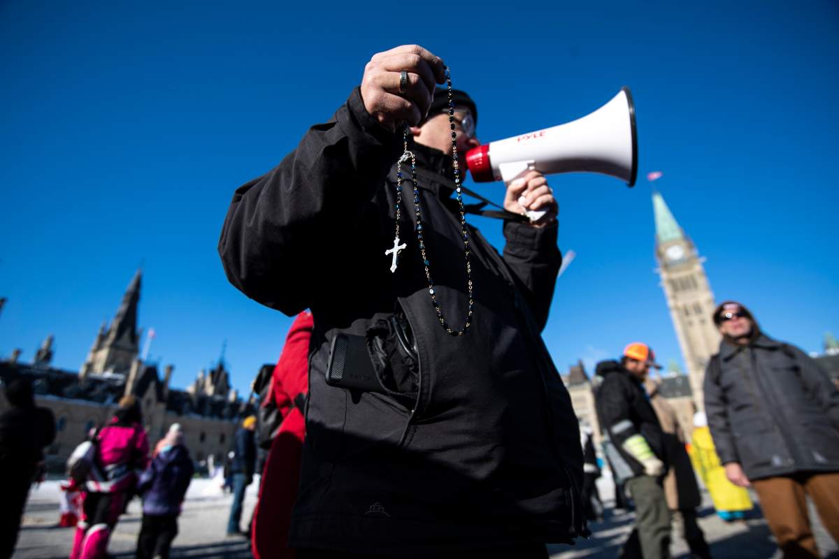 A person leads a group in the saying of the Rosary during a rally against COVID-19 restrictions on Parliament Hill, which began as a cross-country convoy protesting a federal vaccine mandate for truckers, in Ottawa on Sunday, Jan. 30, 2022. THE CANADIAN PRESS/Justin Tang