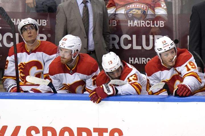 Calgary Flames centre Tyler Pitlick, left, centre Elias Lindholm (28), left wing Johnny Gaudreau (13), and left wing Matthew Tkachuk (19) watch during the closing minutes of the third period of an NHL hockey game against the Florida Panthers, Tuesday, Jan. 4, 2022, in Sunrise, Fla. The Panthers won 6-2.