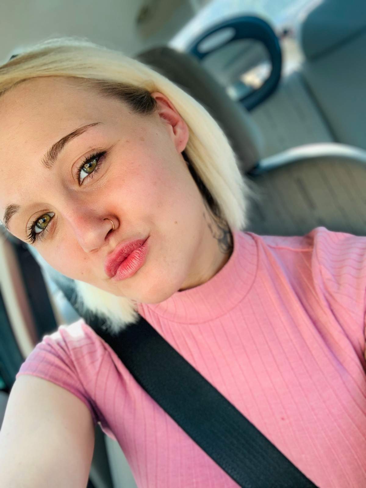 A selfie of Jordan Cashmyer, wearing a pink short sleeved shirt sitting in a car.