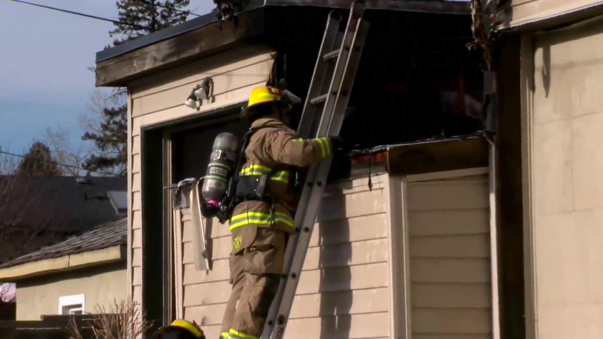 A firefighter works to contain the spread of flames on a garage roof.