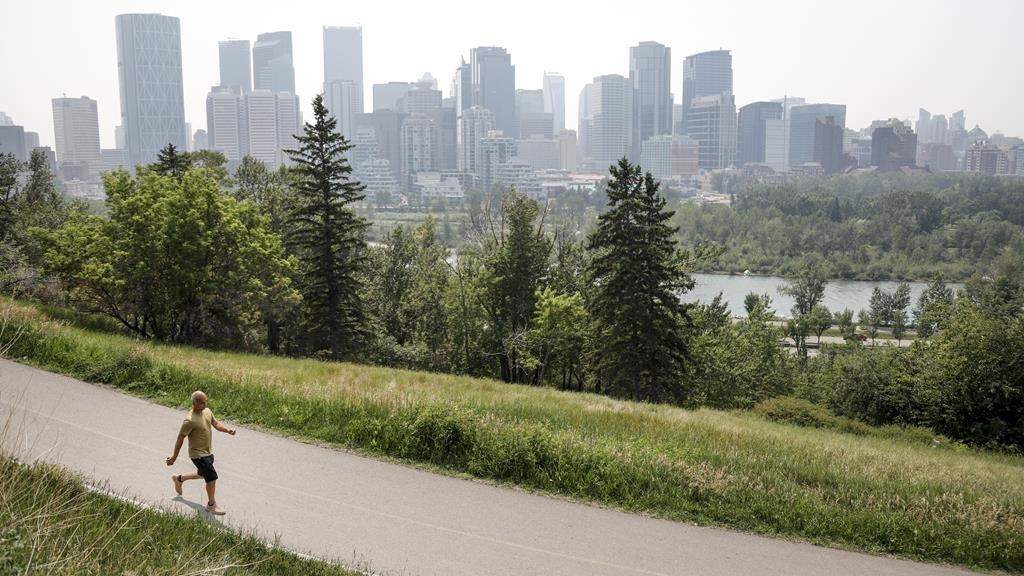 A pedestrian walks on a trail with the Calgary skyline in the background on Thursday, July 15, 2021.