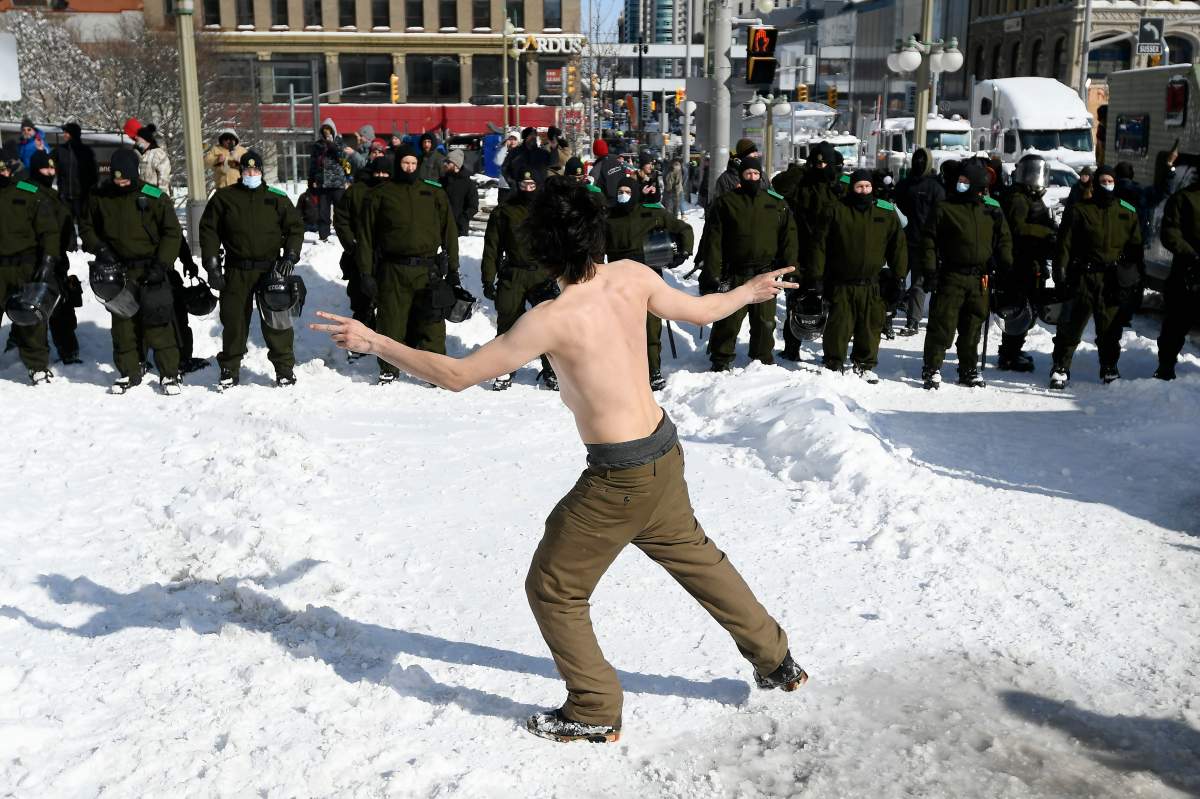 A shirtless protester dances in front of police as they work to bring the protest, which started in opposition to mandatory COVID-19 vaccine mandates and grew into a broader anti-government demonstration and occupation, to an end, in Ottawa, Friday, Feb. 18, 2022. THE CANADIAN PRESS/Justin Tang
