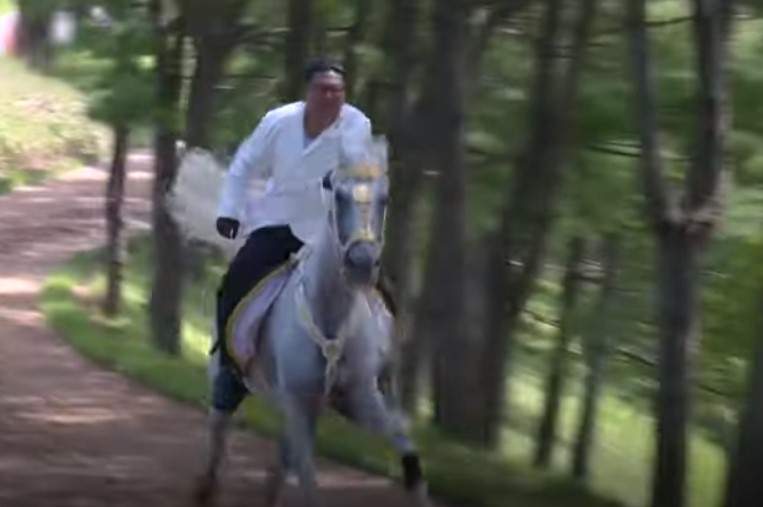 Kim Jong Un is seen on a white horse, riding through the woods