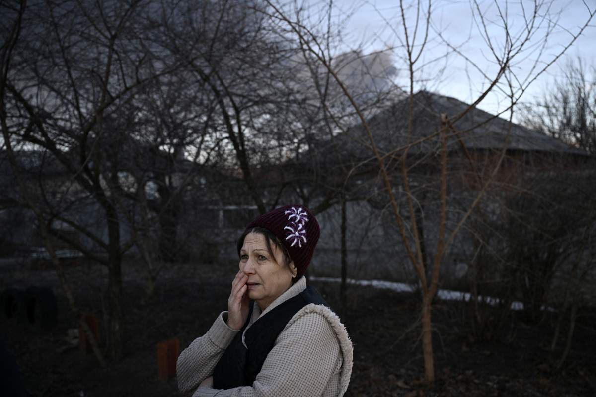 A woman stands in a street as black smoke rises from a military airport in Chuguyev near Kharkiv on February 24, 2022.