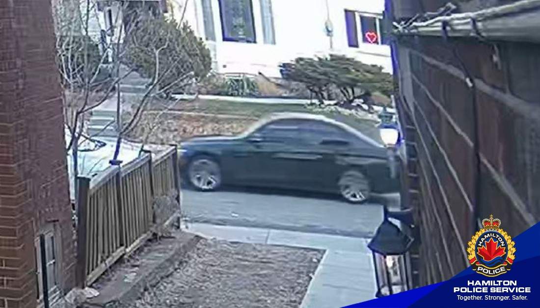 Surveillance camera footage of a dark coloured four-door sedan.