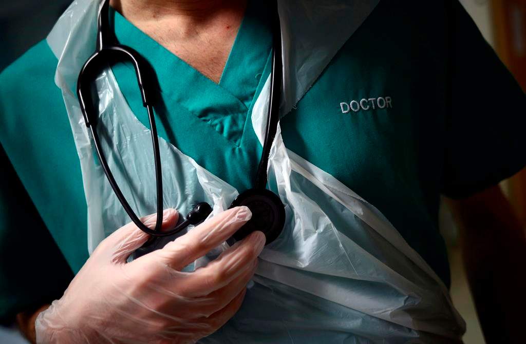 A junior doctor holds his stethoscope during a patient visit at the Royal Blackburn Teaching Hospital, in Blackburn, England, Thursday, May 14, 2020.