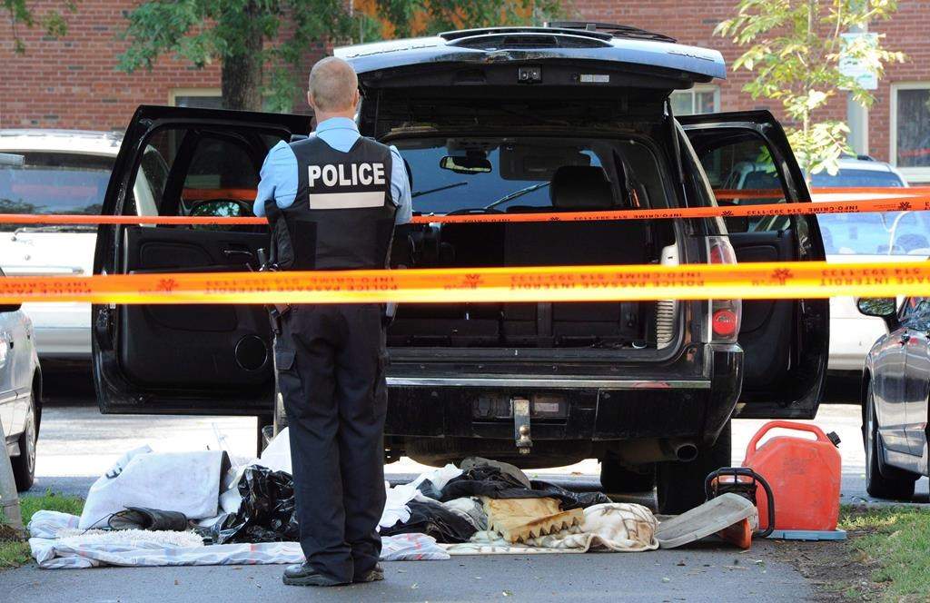 A police officer looks towards a black SUV that has had its contents removed at a crime scene outside the Metropolis in Montreal on Wednesday, Sept. 5, 2012.