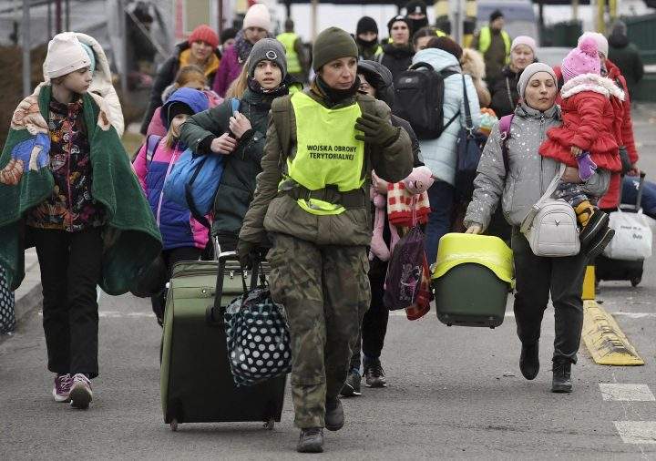 A Polish border guard helps people to carry their belongings at the Ukrainian-Polish border crossing in Korczowa, Poland, Saturday, March 5, 2022.