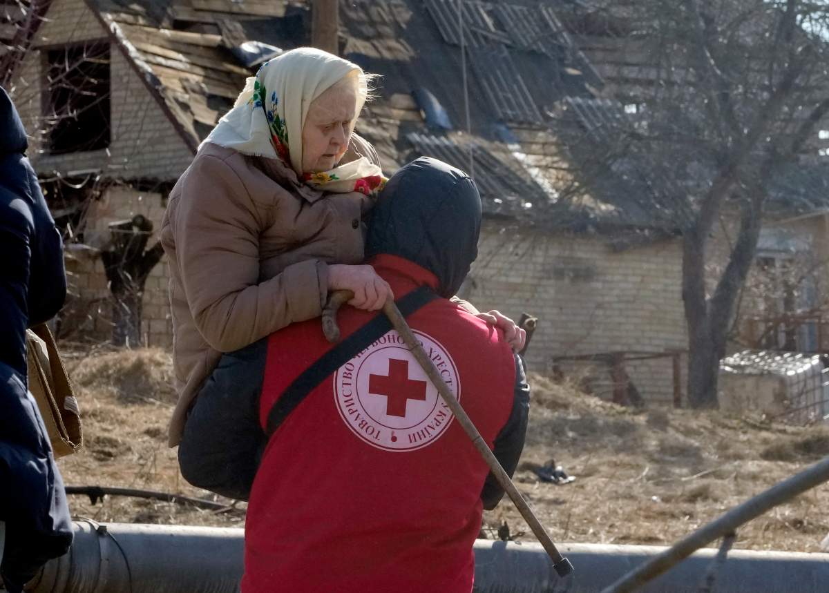 A Red Cross worker carries an elderly women during evacuation in Irpin, some 25 km (16 miles) northwest of Kyiv, Friday, March 11, 2022. Kyiv northwest suburbs such as Irpin and Bucha have been enduring Russian shellfire and bombardments for over a week prompting residents to leave their home. (AP Photo/Efrem Lukatsky)