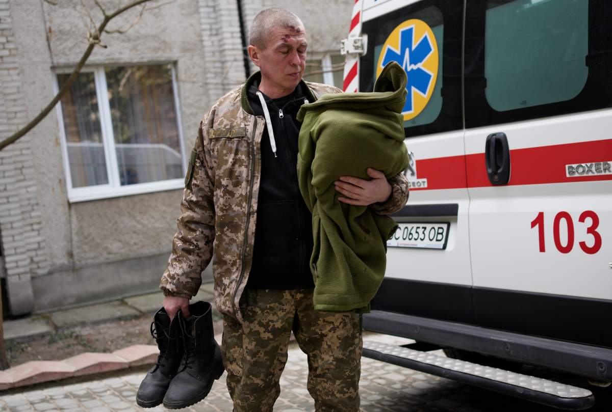 An injured man holds his belongings as he stands next to an ambulance at a local hospital in Novoiavorisk, western Ukraine, Sunday, March 13, 2022. Local officials in western Ukraine say a Russian airstrike has hit a military training base that has hosted NATO drills. (AP Photo/Bernat Armangue)