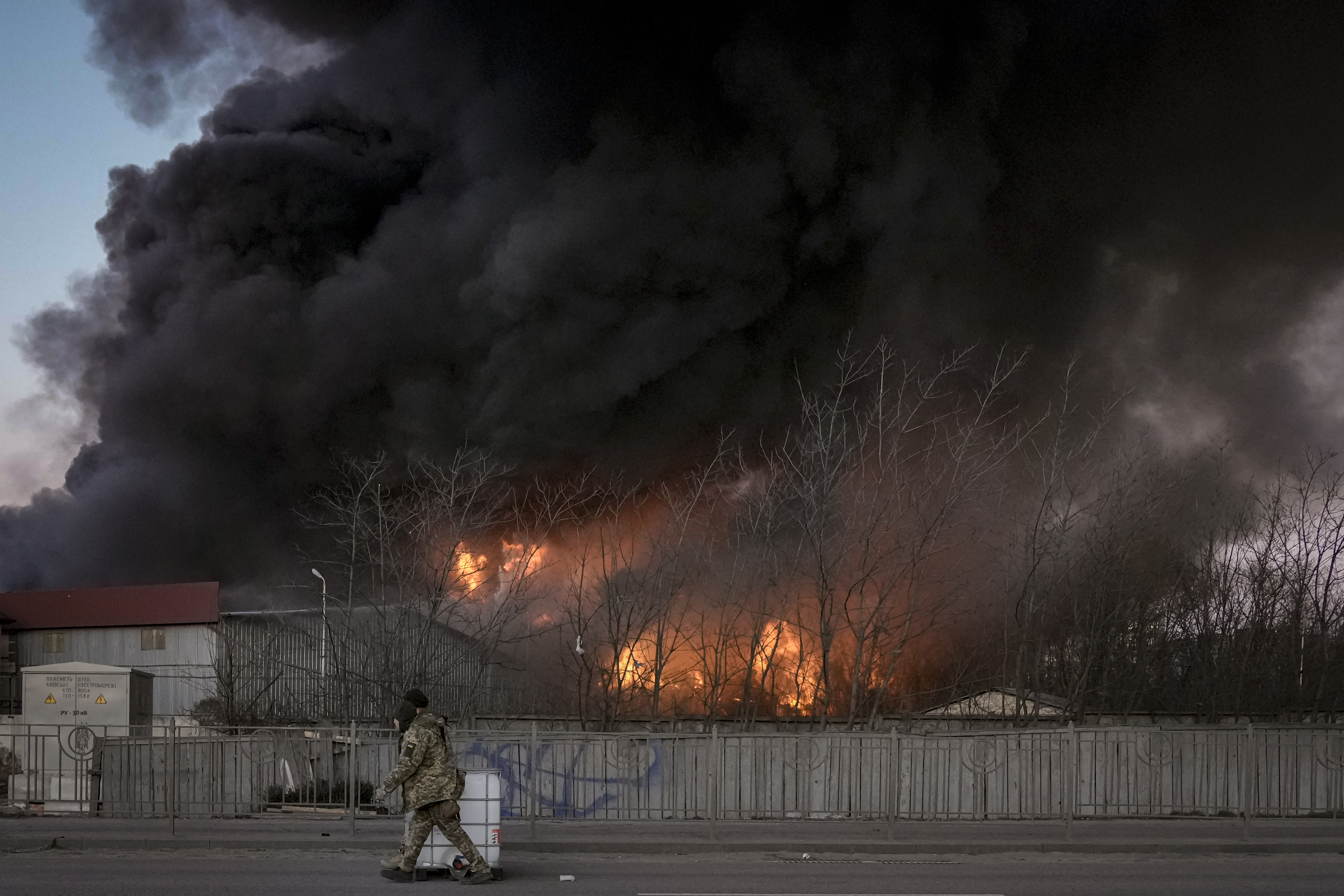 Ukrainian servicemen carry containers backdropped by a blaze at a warehouse after a bombing on the outskirts of Kyiv, Ukraine, Thursday, March 17, 2022. Russian forces destroyed a theater in Mariupol where hundreds of people were sheltering Wednesday and rained fire on other cities, Ukrainian authorities said, even as the two sides projected optimism over efforts to negotiate an end to the fighting. (AP Photo/Vadim Ghirda).