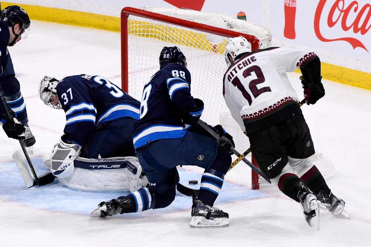 Arizona Coyotes’ Nick Ritchie (12) scores on Winnipeg Jets’ goaltender Connor Hellebuyck (37) as Nate Schmidt (88) defends during the third period of NHL action in Winnipeg on Sunday March 27, 2022.