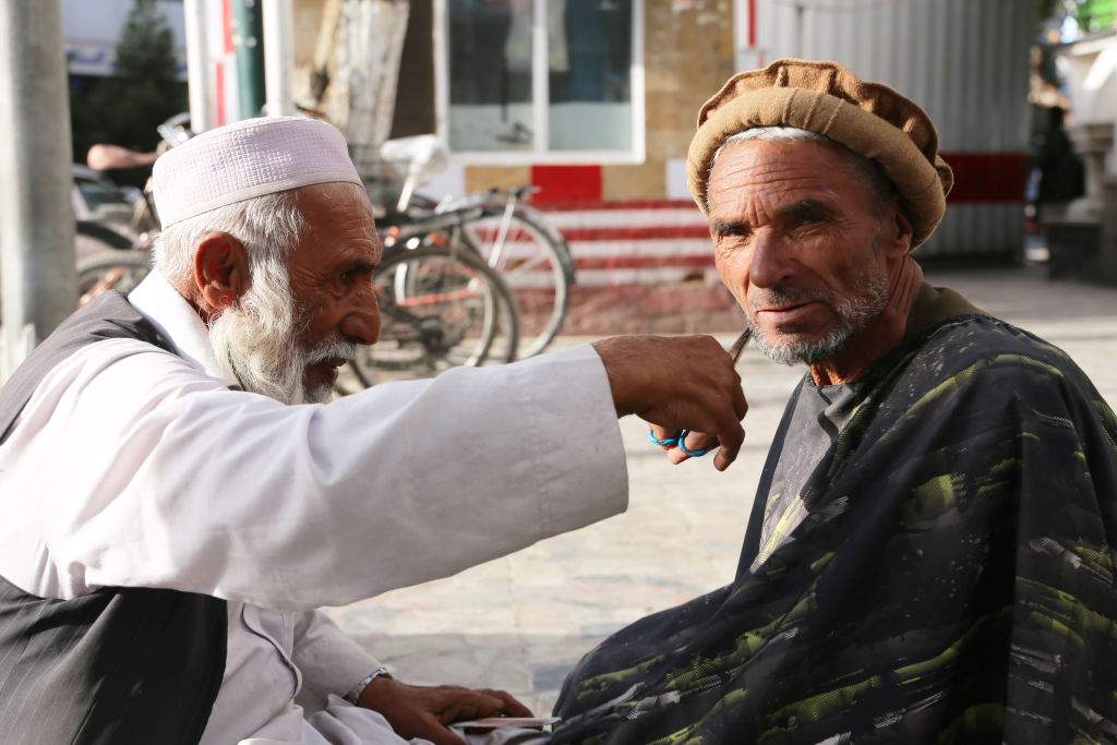 A mobile barber trims a beard of his customer at Haji Yaqub square as people continue their daily lives in Kabul, Afghanistan