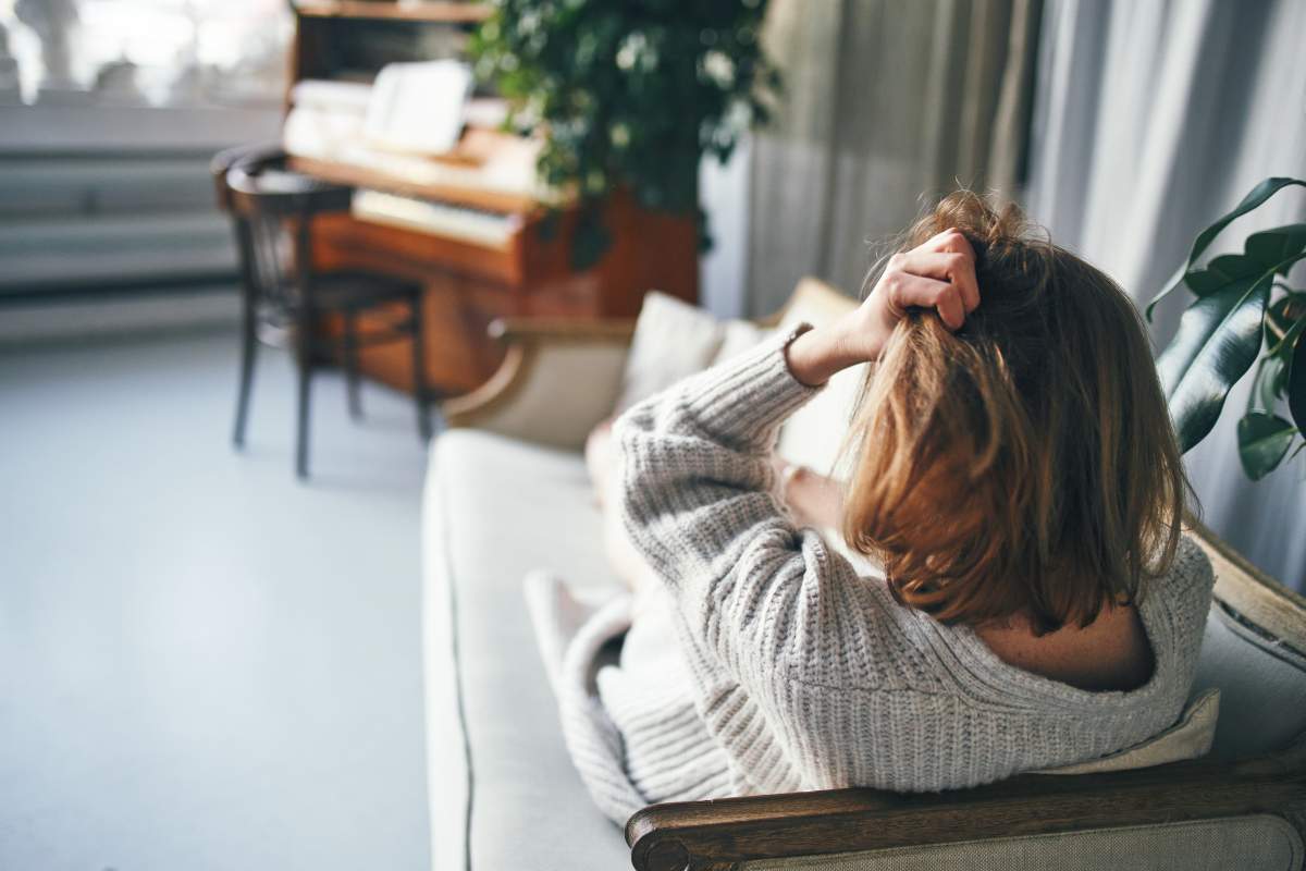 A file photo of a woman with her back to the camera is lying on a sofa in a beautiful room with a piano, her hand holding her head.