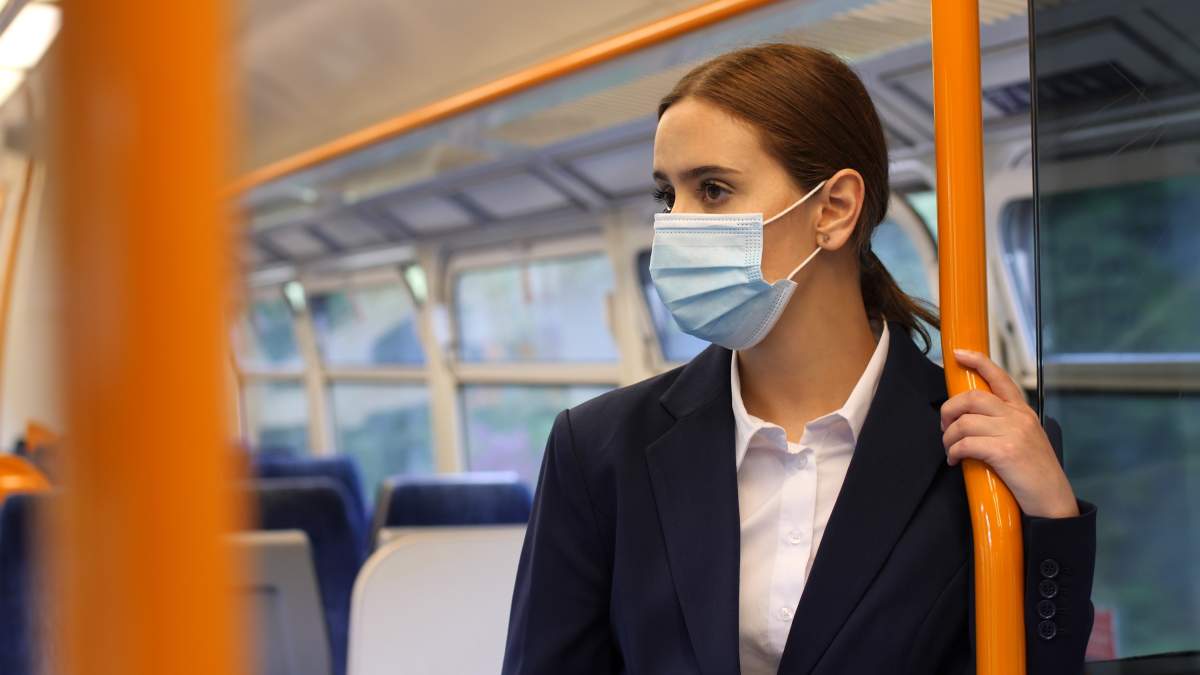 Young woman on a train wearing a protective mask, she is standing holding the rail.