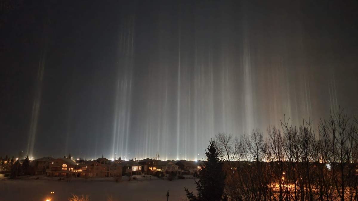 Light pillars dazzle in prairie night sky.
