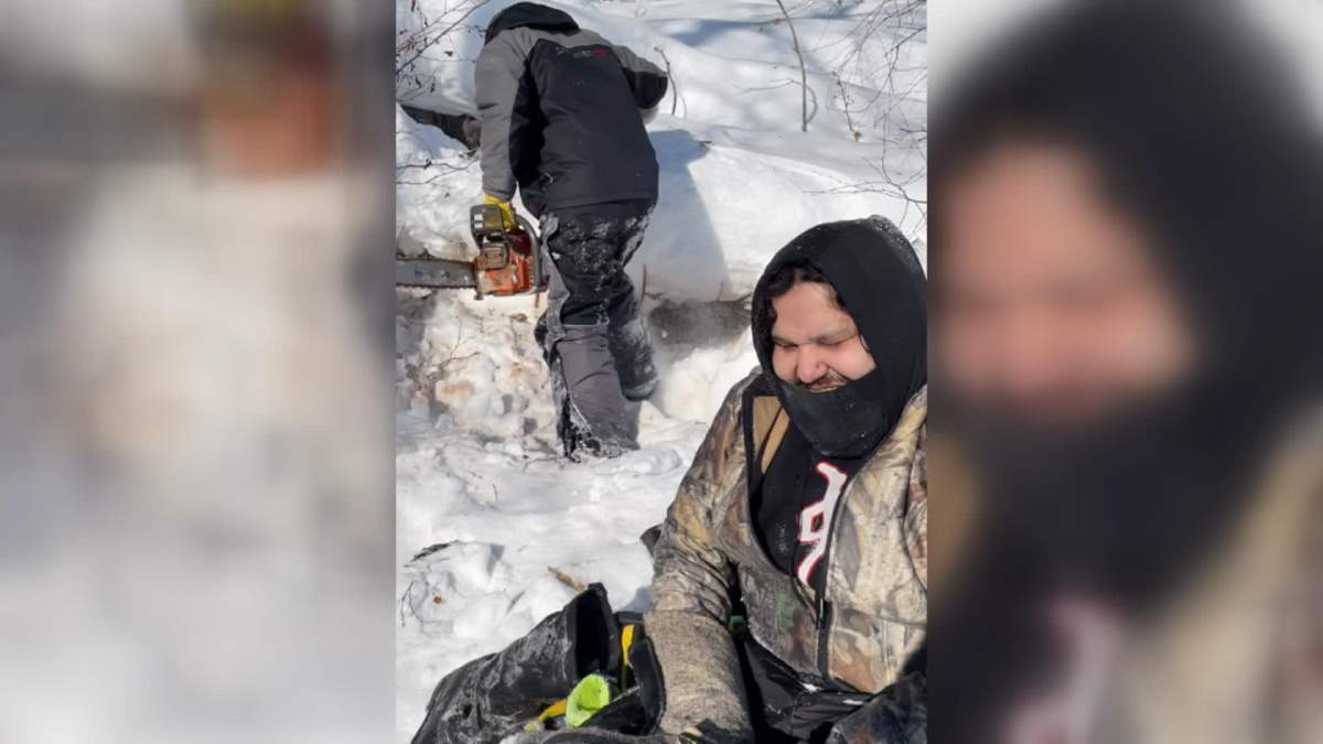 Julian Herman dries out his gear as Ron Hyggen prepares to saw wood after they got stuck for the first time on Triveet Lake in northern Saskatchewan in a February 2022 handout photo. Three cousins used traditional trapping skills and Old Spice body spray to survive a freezing night on Triveet Lake in northern Saskatchewan after their snowmobiles were stuck in slush. 