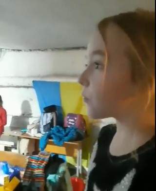 A young girl is seen in profile, standing in a bunker, singing to the crowd.