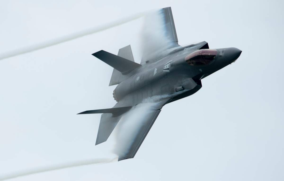 The F-35 fighter jet is visible close up flying against a grey sky.