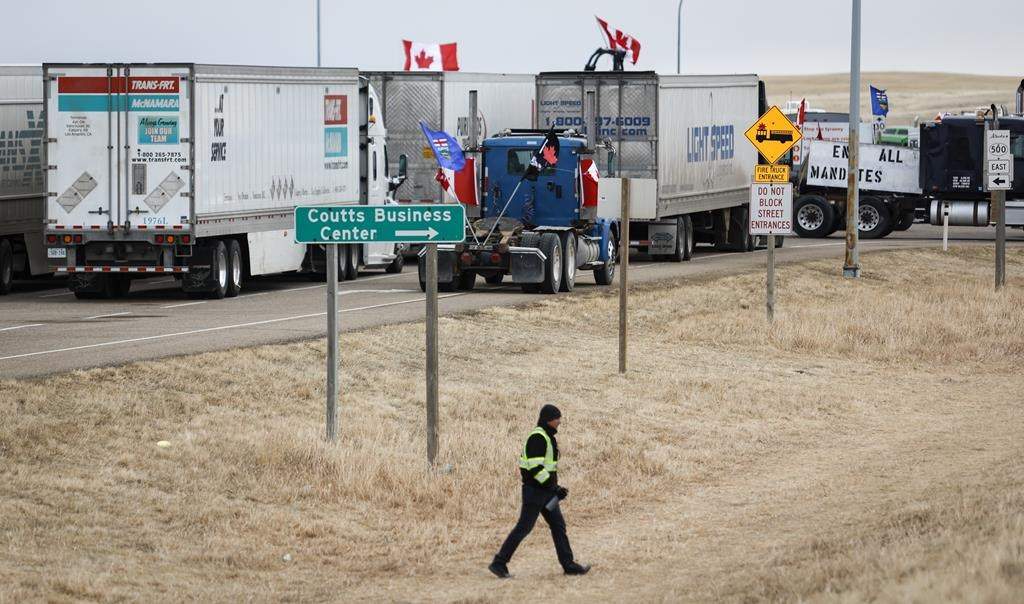 Anti-mandate demonstrators gather as a truck convoy blocks the highway at the busy U.S. border crossing in Coutts, Alta., Monday, Jan. 31, 2022. One of four men charged with conspiracy to commit murder at a border blockade protest in southern Alberta has run into a roadblock in his desire to set an early trial date. THE CANADIAN PRESS/Jeff McIntosh.
