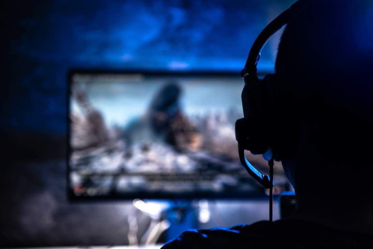 A stock photo of a gamer wearing headphones, playing video games late at night.