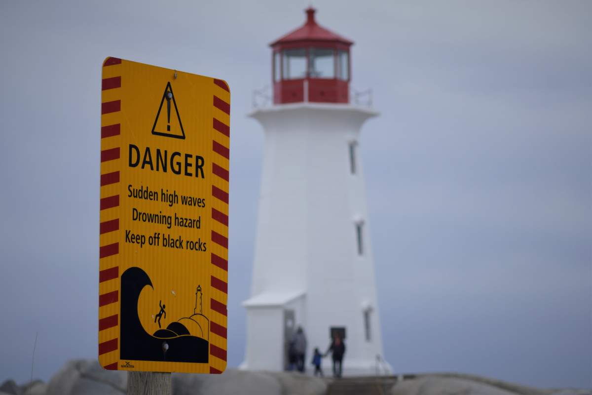 A warning sign stands near the Peggy’s Cove lighthouse.