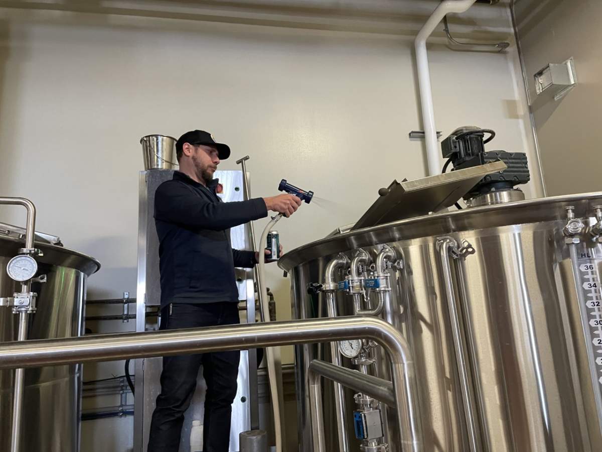 A male worker aims a hose into the top of a large steel vat, where spent grain is being cleaned out during the process of making beer.