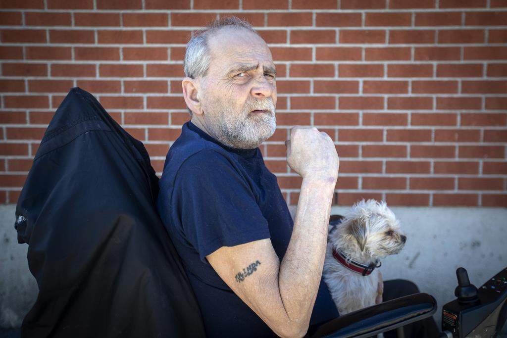 Will Towell holds his miniature terrier on his lap outside his temporary housing in Kingston, Ont., on Monday May 9, 2022.