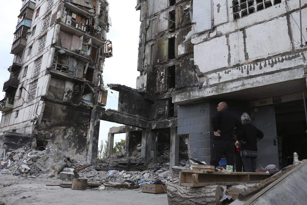 Local residents stand at the side of damaged during a heavy fighting buildings in Mariupol, in territory under the government of the Donetsk People’s Republic, eastern Ukraine, Friday, May 13, 2022.