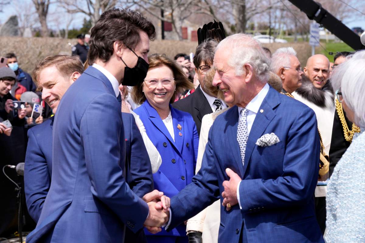 a photo of Justin Trudeau and Prince Charles shaking hands. Both are wearing blue suits.