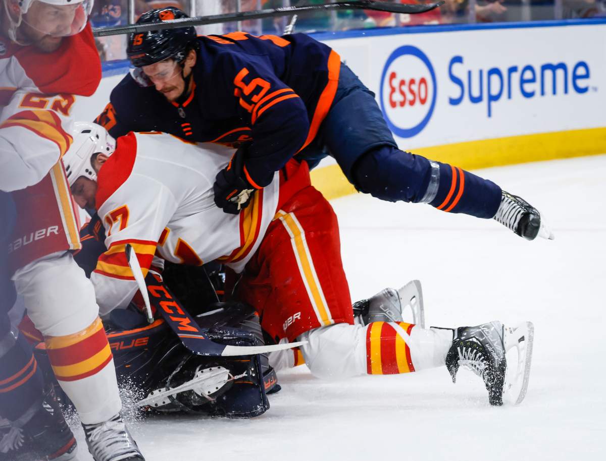 Calgary Flames forward Milan Lucic, centre, crashes down on Edmonton Oilers goalie Mike Smith, hidden, as winger Josh Archibald joins in during third period NHL second round playoff hockey action in Edmonton, Sunday, May 22, 2022.