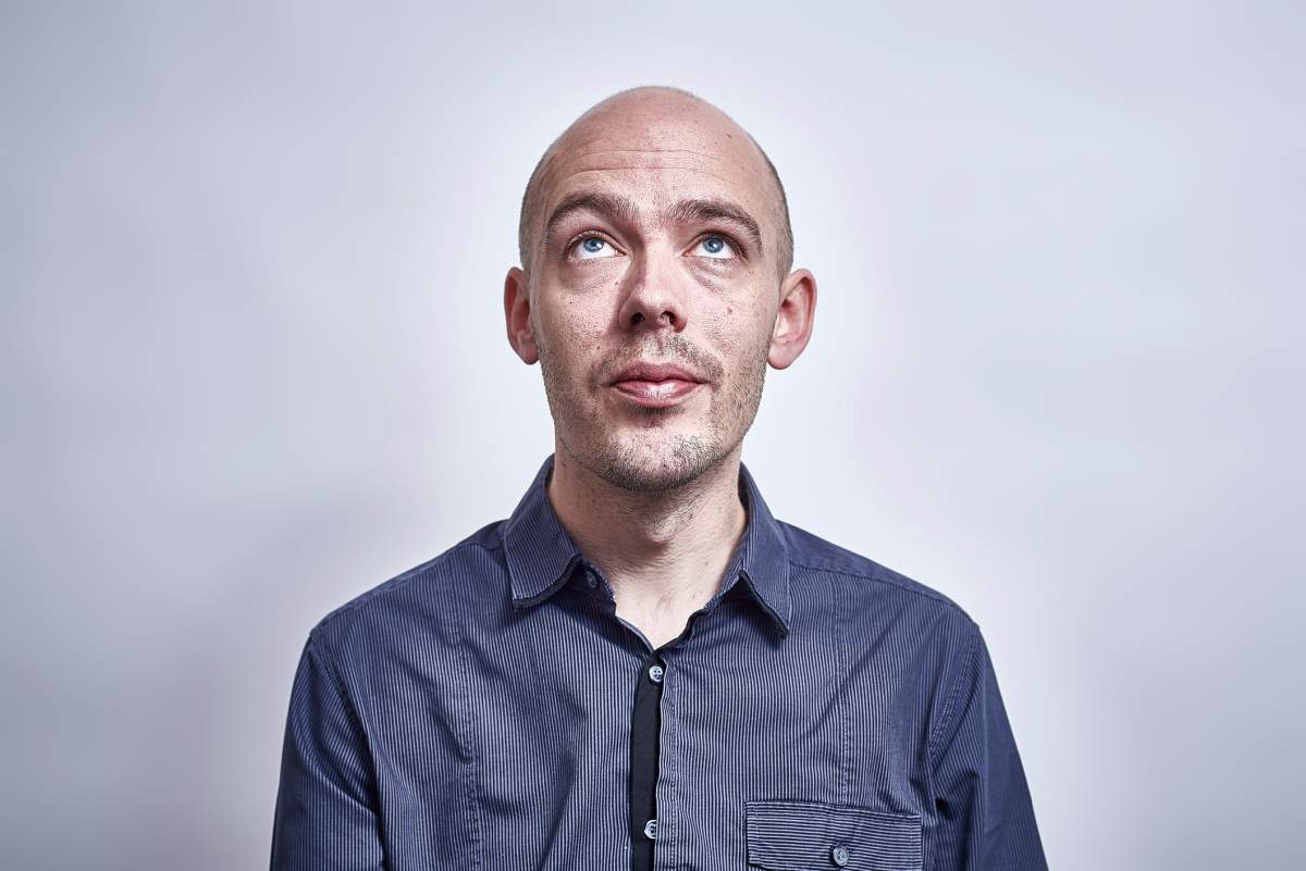 A studio portrait of a early thirties bald headed male looking up.