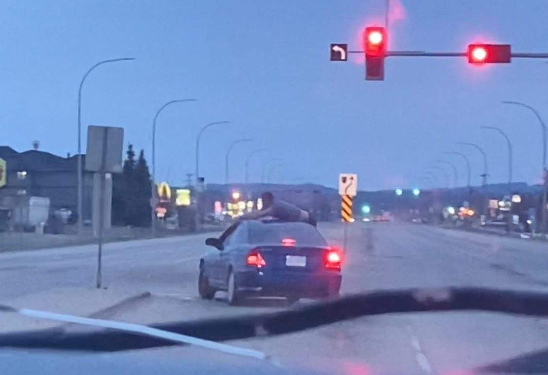 Shot of a man riding on the roof of a car vehicle after a hit-and-run in Whitecourt, Alta., on May 2, 2022.