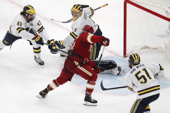 Denver’s Carter Savoie (8) gathers the puck for the winning goal on Michigan’s Erik Portillo (1) in overtime during an NCAA men’s Frozen Four semifinal hockey game, Thursday, April 7, 2022, in Boston.