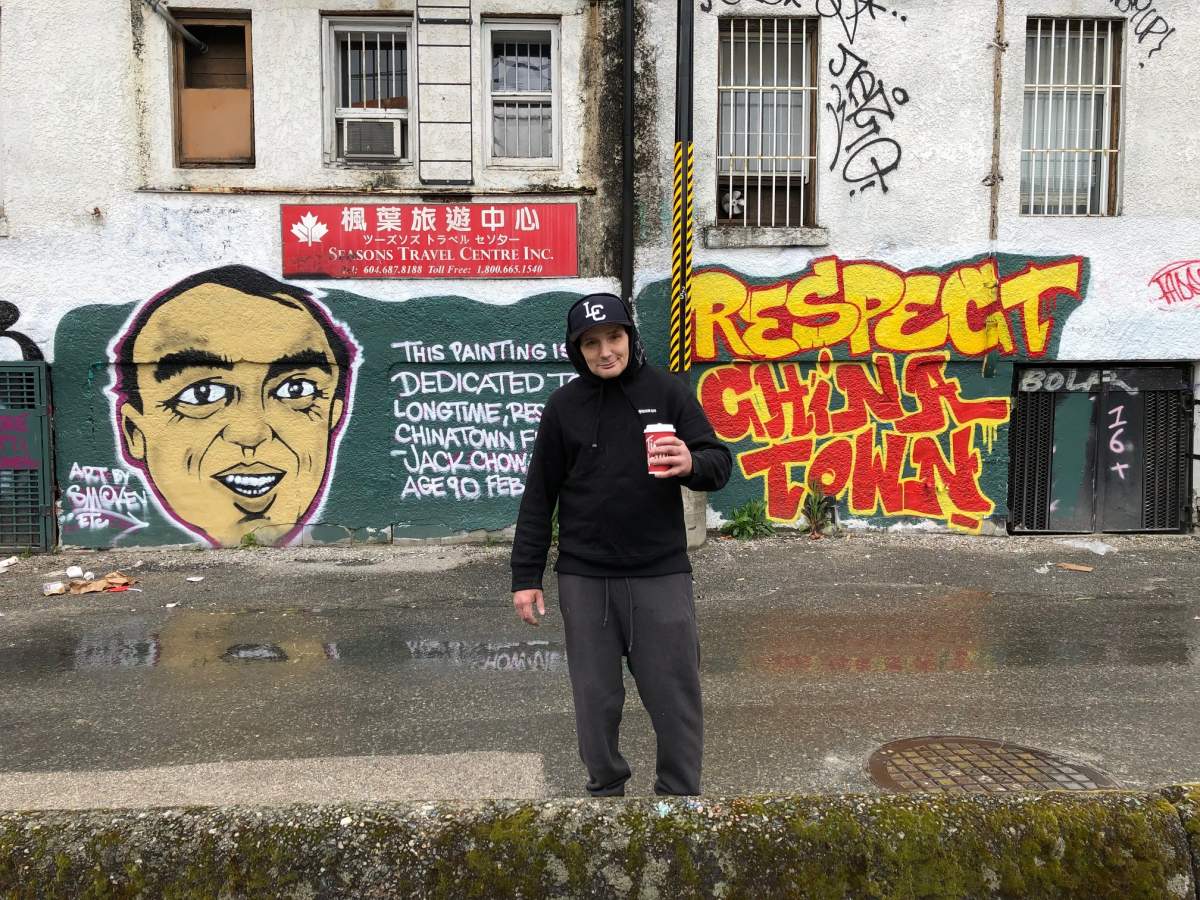 Well-known Downtown Eastside street artist Smokey D poses with a mural he painted in Chinatown urging respect.