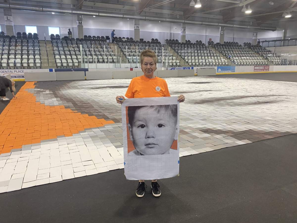 Minda Burley stands at the centre of the QPlex in Quispamsis, N.B., holding a copy of the only photo she has of herself as a baby.