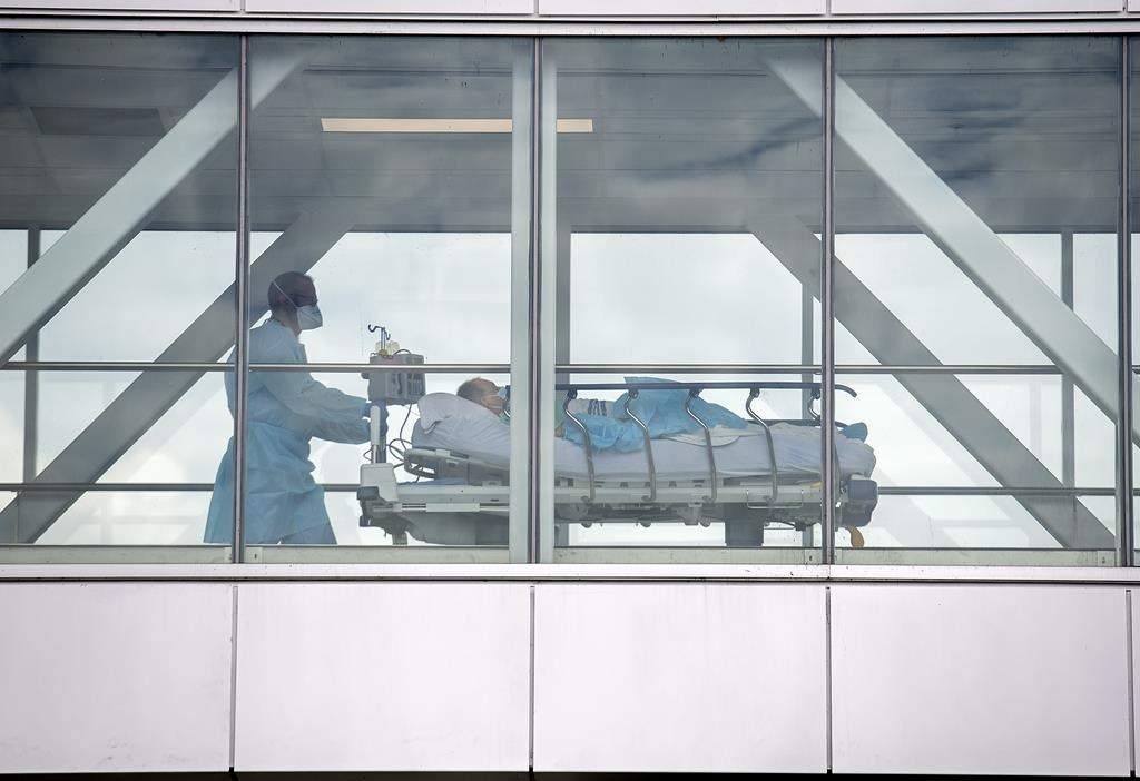 A health-care worker pushes a patient across a connecting bridge at a hospital in Montreal, Thursday, July 14, 2022, as the COVID-19 pandemic continues in the province. THE CANADIAN PRESS/Graham Hughes.