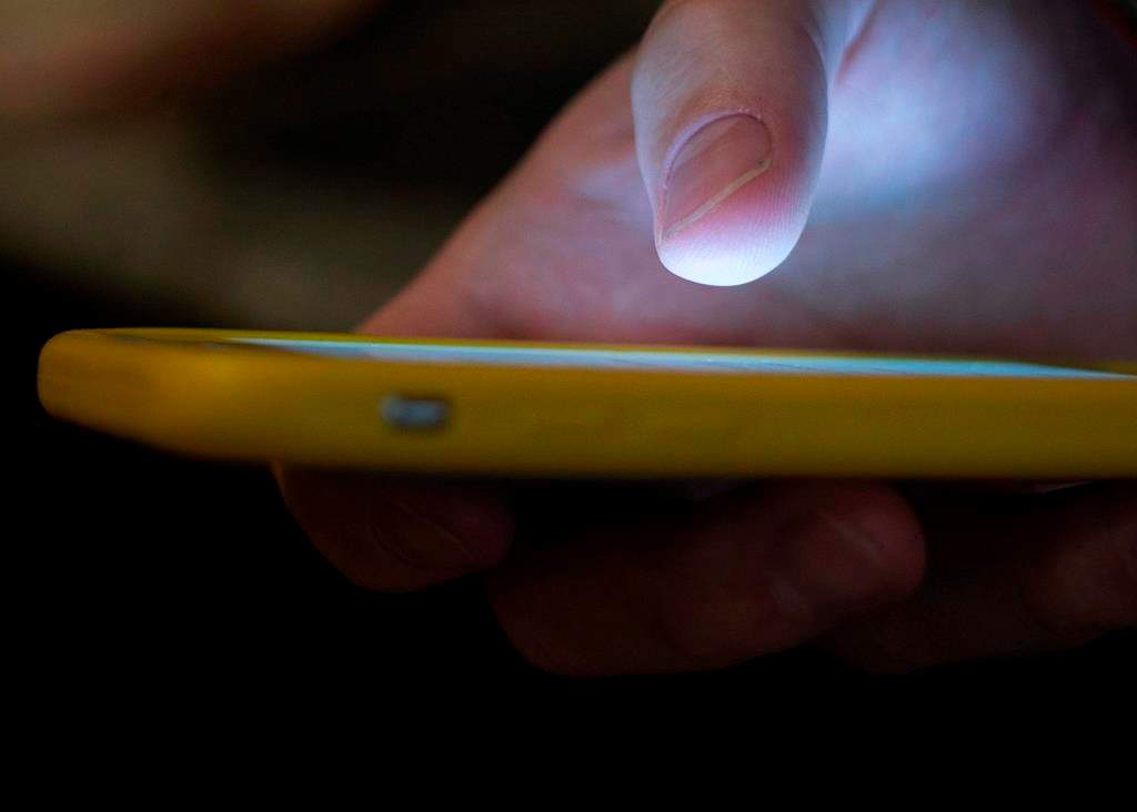 In this Aug. 11, 2019, file photo, a man uses a cell phone in New Orleans. Calgary police are warning about a new text scam that uses threats and graphic imagery to get funds.