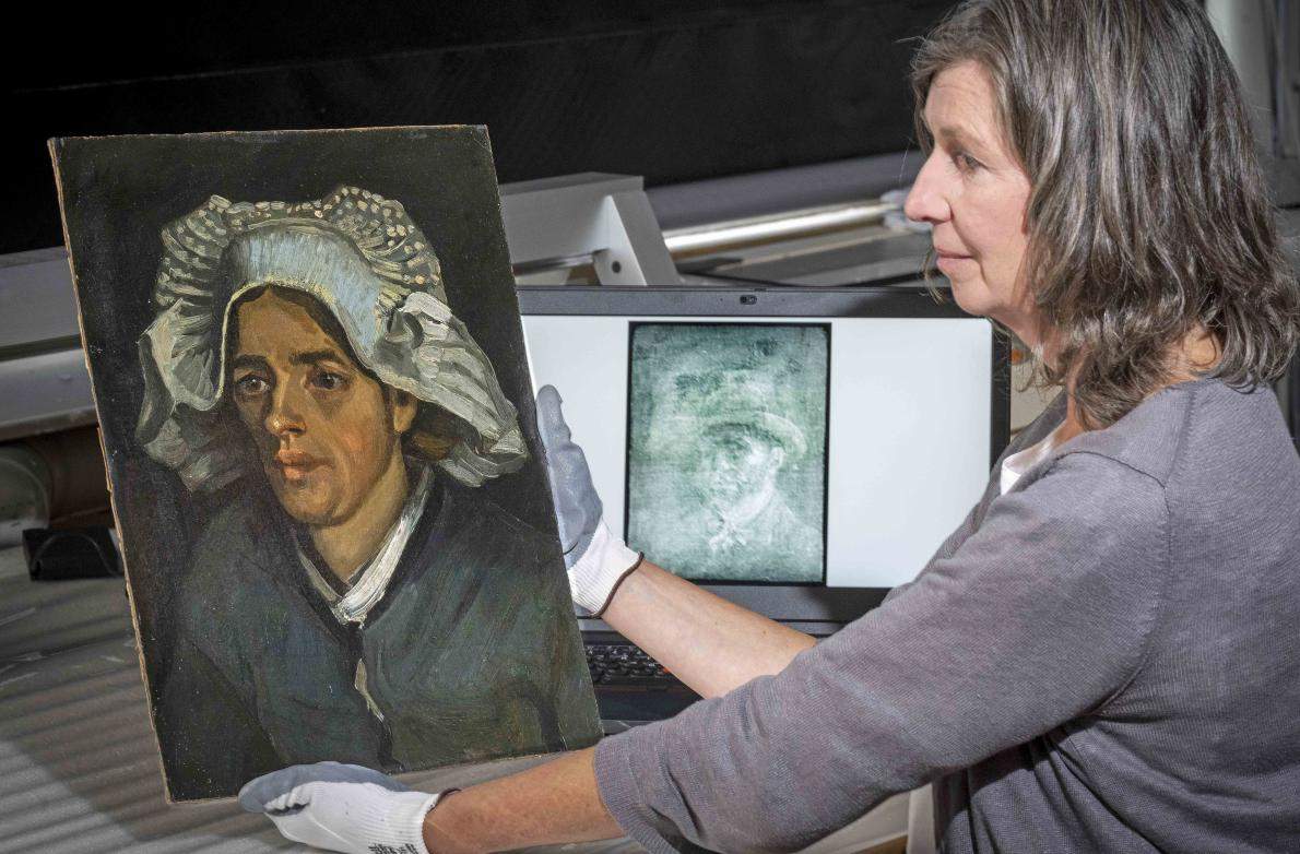Senior Conservator Lesley Stevenson wears white gloves as she views "Head of a Peasant Woman" beside an X-ray image of the hidden Van Gogh self-portrait.