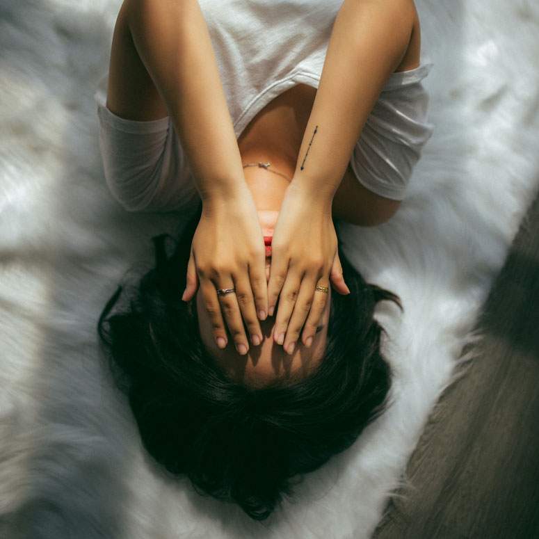 A woman lying down with her hands over her face