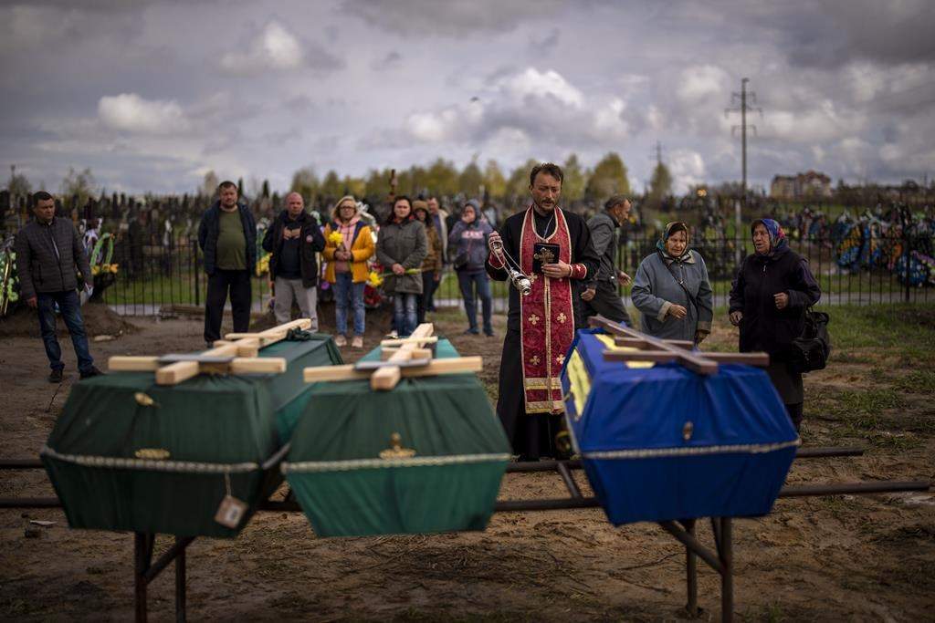 Priest blesses remains of three people who died during the Russian occupation of Bucha, on Wednesday, April 27, 2022. (AP Photo/Emilio Morenatti)
