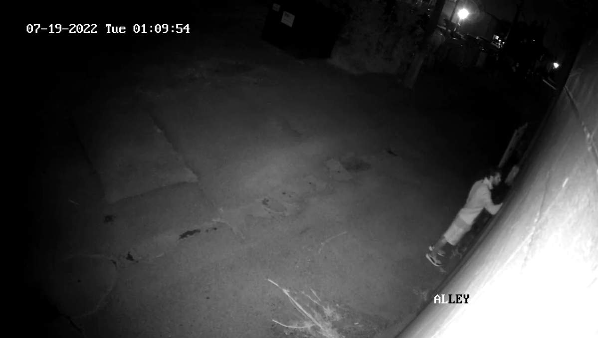 Surveillance footage still from July 19, 2022 showing a man writing on a wall in an alley in west Edmonton.