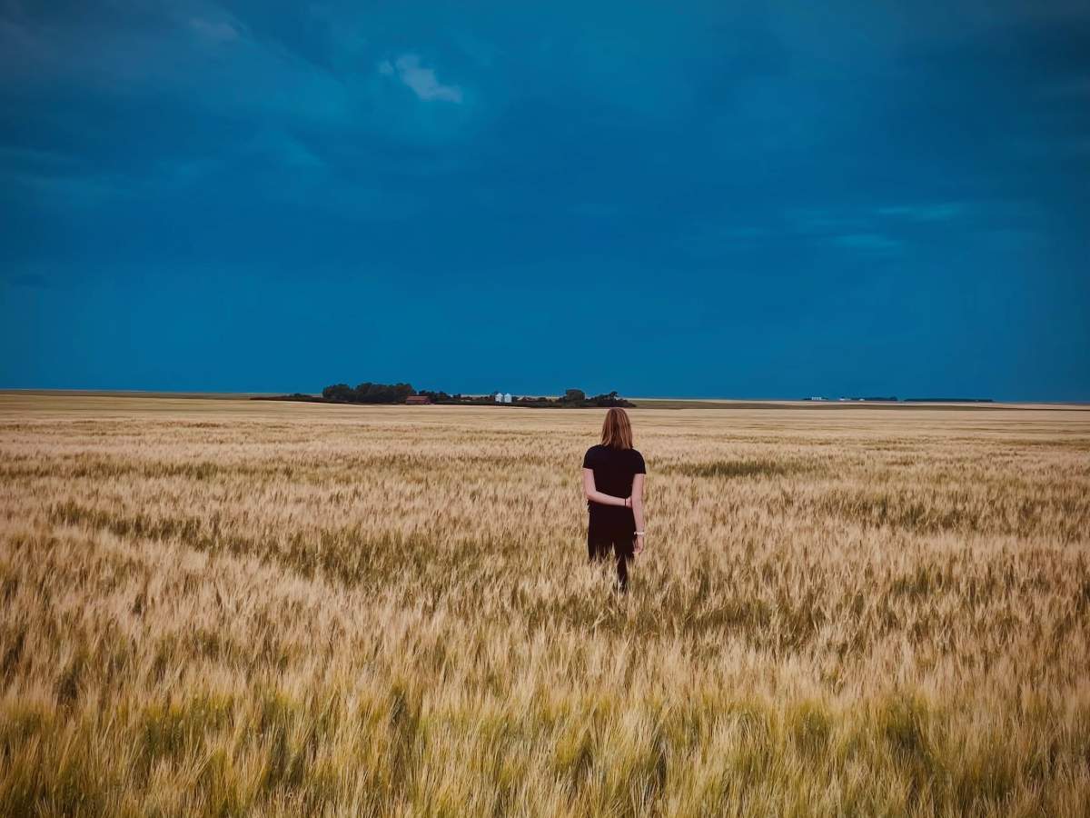 woman in white field looking at dark blue sky