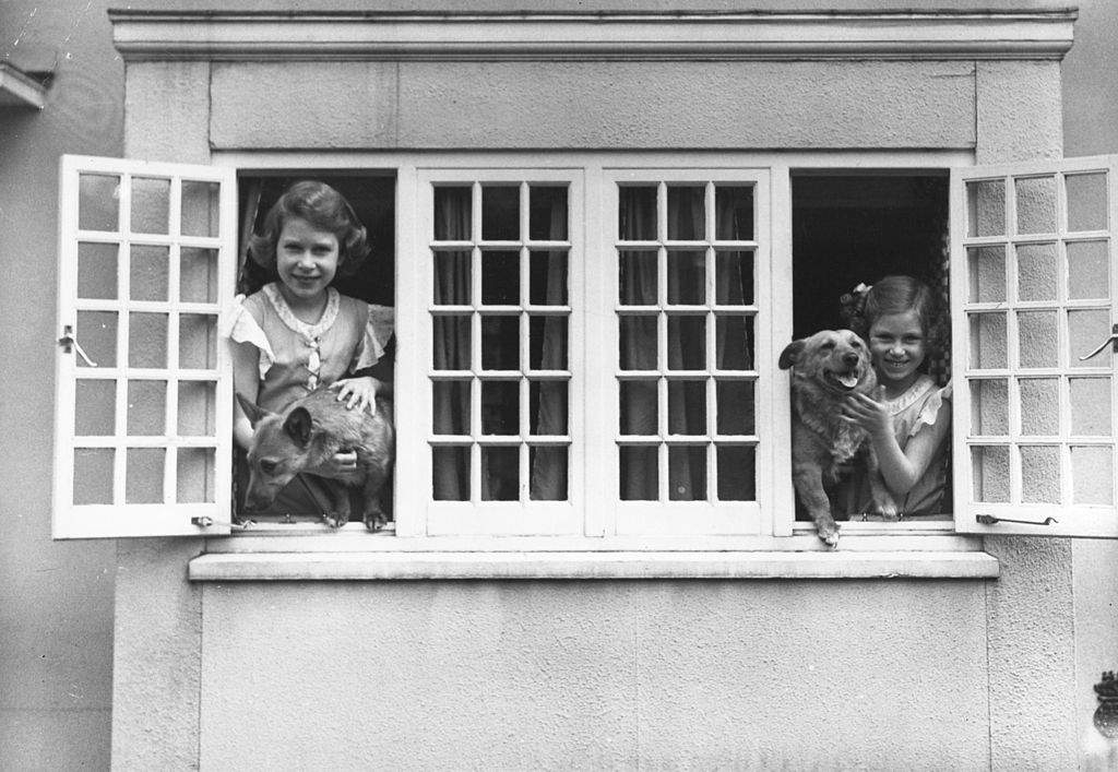 The Royal Princesses Elizabeth and Margaret (1930 - 2002) at the windows of the Royal Welsh House with two Corgi dogs, June 1936.