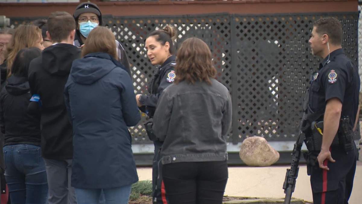 A Regina Police Service officer tells concerned parents there were no injuries reported. An officer wearing a carbine long gun stands nearby. RPS say nine officers responded inside the high school after the gun report came in Friday morning. Over a dozen officers secured the entire school property.