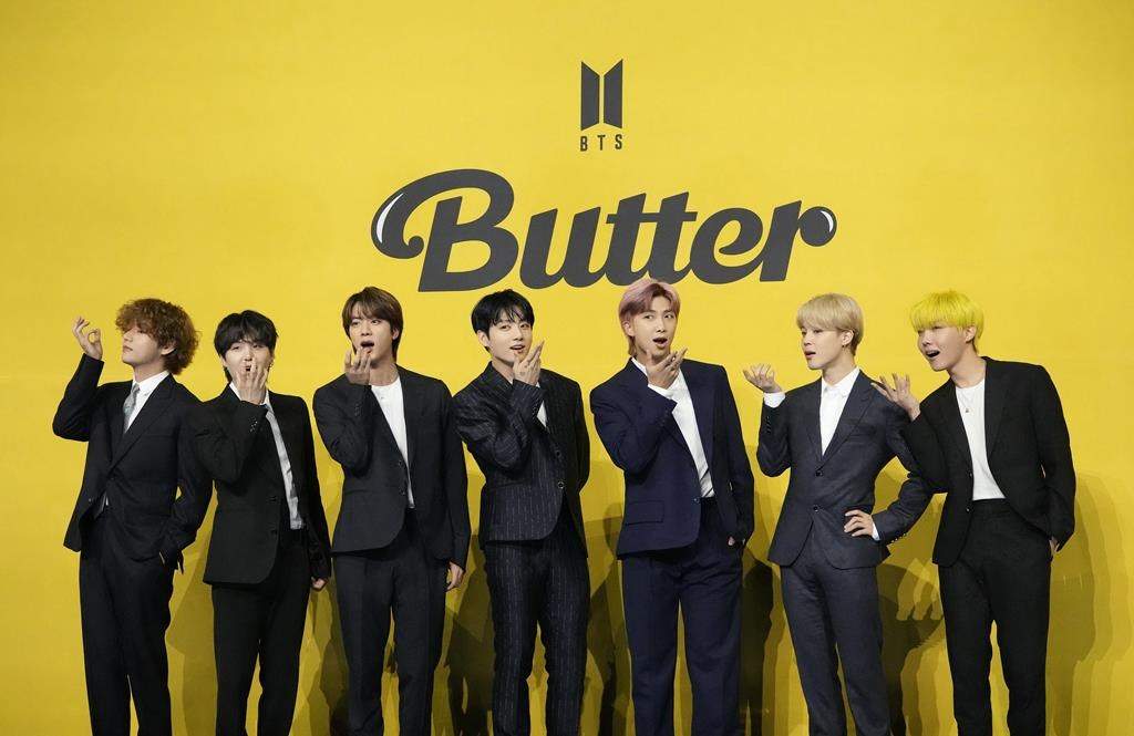 The members of BTS standing in front of a promotional banner for their song 'Butter.'