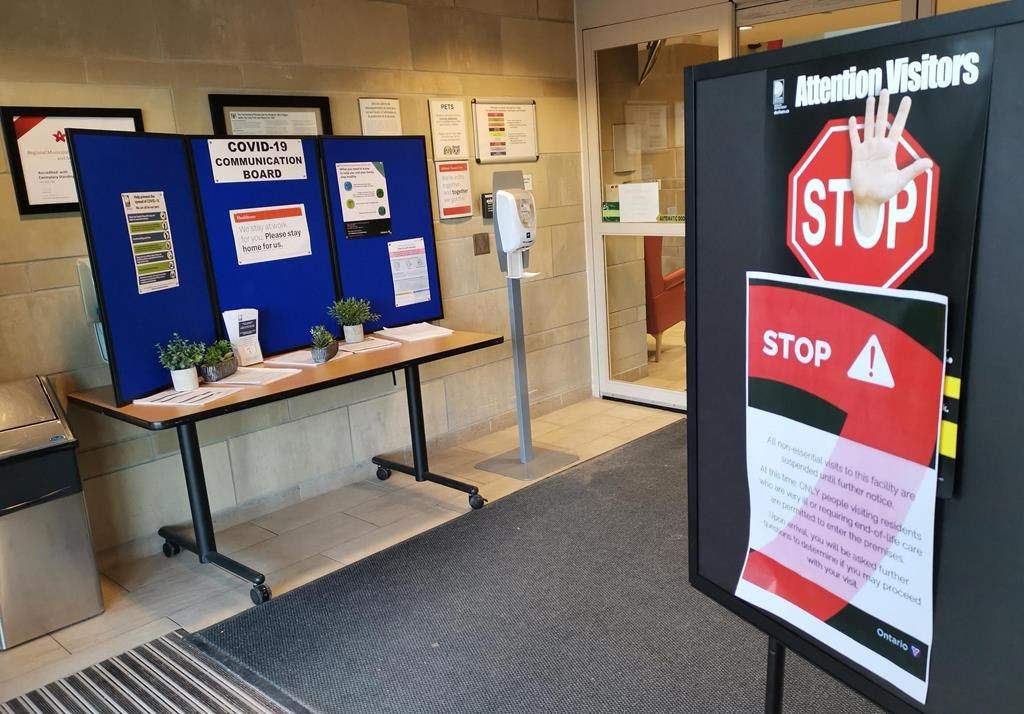 Signs and information about COVID-19 along with a hand sanitizing station are shown inside the doors of the Hillsdale Terraces Long-Term Care home in Oshawa, Ont., on Sunday, April 5, 2020. Ontario has quietly changed mask rules for long-term care homes, no longer requiring visitors or caregivers to wear them when alone with a resident in their room. 