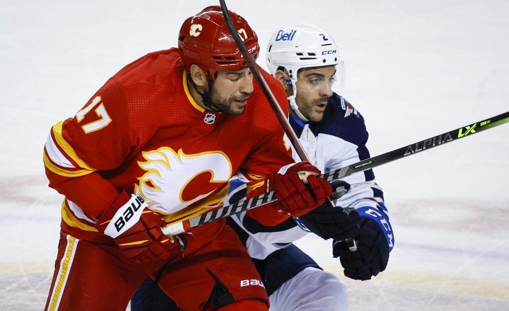 Winnipeg Jets defenceman Dylan DeMelo, right, checks Calgary Flames forward Milan Lucic during second period NHL pre-season hockey action in Calgary, Friday, Oct. 7, 2022. Calgary Flames winger Milan Lucic reached a career 1,100 NHL games played Thursday with a live audience on hand for that milestone. THE CANADIAN PRESS/Jeff McIntosh