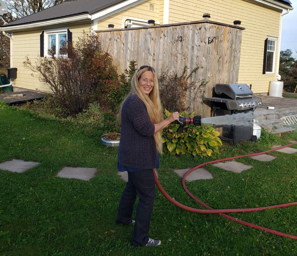 Maureen Blake holds a fire hose as she fills up a rain barrel to use due to lack of water from ongoing power failures following Hurricane Fiona